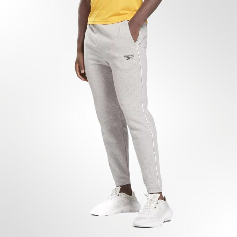 A man wearing the Reebok Workout Ready Piping Sweatpants, showcasing their comfortable, relaxed fit and stylish details